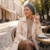 A customised elastic headband in grey is worn by a woman sitting at a café table outdoors, enjoying a coffee.