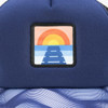 A trucker cap featuring a navy blue design with a full colour patch depicting a sunset over a pathway.