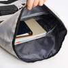A roll top backpack in grey with a spacious interior, holding notebooks and a folder. Features a brand logo.