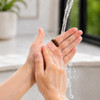 A dark ceramic ring is held between two hands under running water, with a blurred background.