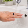 A black carbon fibre NFC ring is being rinsed under running water in a sink. 