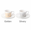Two ceramic coffee mugs, one in golden and the other in silvery, each with matching saucers and a logo.