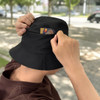 A black bucket hat with a card pocket, held by a person in a casual setting.