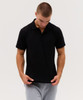 A black polo shirt is displayed, featuring a classic collar and short sleeves. The model wears grey sweatpants.