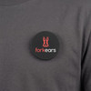 A round black magnetic badge featuring a logo and placed on a grey shirt.