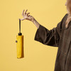 A yellow compact umbrella held by a person, with a plain background and a visible logo on the umbrella.