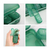 A green seven-day pill organiser with compartments for each day, featuring a clear lid and individual openings.