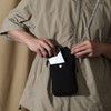 A minimalist black crossbody phone bag being held by a person, with a phone partially inserted into its pocket.