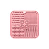A pink, four-section dog enrichment lick mat featuring various textured patterns, including paw prints and bones, with a central hole.