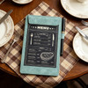 A5 magnetic clipboard in teal with a menu design, placed on a patterned tablecloth beside a pen and plates.
