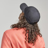 A black cap is worn backwards on the head of a person with curly hair, set against a neutral background.