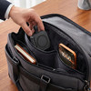A black magnetic wireless charging station is placed inside a dark bag alongside a phone and a notebook.