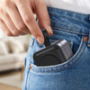 A compact grey magnetic wireless charging station being placed in a pocket of denim jeans.