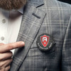 A round button badge, 44mm in size, featuring a shield design, pinned on a grey checked blazer.