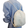 A cream drawstring bag is worn on the back, secured by matching drawstrings, against a light blue shirt.