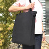 A foldable black calico tote bag with handles, held by a person against a backdrop of greenery.