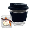 A clear glass coffee cup with a black lid and sleeve, beside a packet of mixed jelly lollies in various colours.