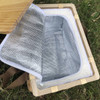 A wicker picnic cooler basket in natural wood with a silver insulated interior and an open lid, resting on grass.