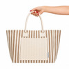 A hand holds a striped brown and cream tote bag featuring a front pocket and dual handles.