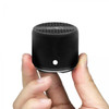 A compact black Bluetooth speaker held in a hand, featuring a textured top and a minimal design.