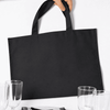 A black picnic backpack with sturdy handles, placed near glasses and tableware. It has a simple, minimalistic design.
