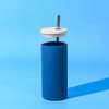 A drink bottle with a blue silicone exterior, wooden lid, and metal straw on a blue background.