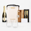 A champagne bottle, insulated bag, wooden chopping board, knife set, two glasses, and a blank card. The colours are neutral and earthy.