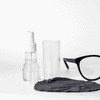 An eye glass cleaner set featuring a spray bottle, a clear container, a black cleaning cloth, and a pair of black glasses.
