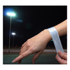 A reflective slap wristband in white is worn on a wrist, illuminated by outdoor lights at night.