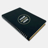 A black spiral notebook with a circular logo on the cover, featuring a shiny gold accent.