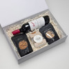 A drink bottle, a bottle of red wine, pretzels, salted nuts, and caramel fudge in a gift box.