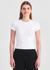 A white baby tee with short sleeves, paired with black trousers. The model stands against a neutral background.