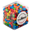 A clear cube filled with colourful chocolate-coated candy, including red, blue, yellow, green, and brown M&Ms.