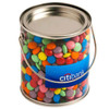 A clear PVC bucket filled with colourful choc beans, featuring a metal lid and a handle. Includes branding on the front.