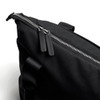A black tote bag features a zip closure with leather zip pulls and a sturdy handle. It has a sleek, minimal design.