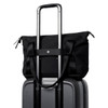 A black tote bag perched on top of a grey suitcase, featuring handles and a strap for carrying.