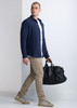 A navy long sleeve shirt worn by a man carrying a black duffle bag, complemented by beige pants and sneakers.