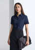 A woman wearing a navy short sleeve shirt, paired with a black skirt and holding a large handbag.