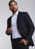 A man in a black suit jacket over a white shirt, standing confidently against a light grey background.