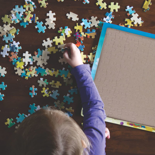 A child’s hand sorting colourful jigsaw puzzle pieces on a table, with an empty puzzle frame nearby.