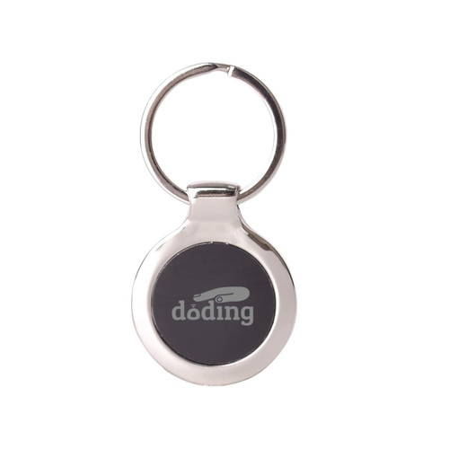 A metallic keyring with a circular design and a dark central area, featuring a branding logo.