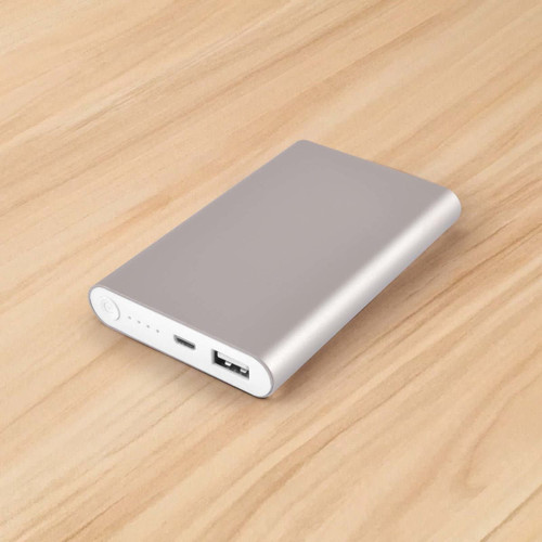 A silver power bank with a USB port on a wooden surface, featuring a sleek, minimal design and a logo.