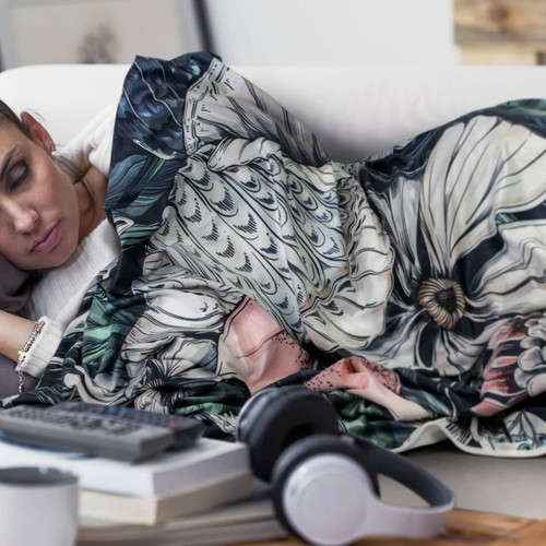 A decorative blanket featuring vibrant floral patterns in various colours, draped over a person lounging on a couch.