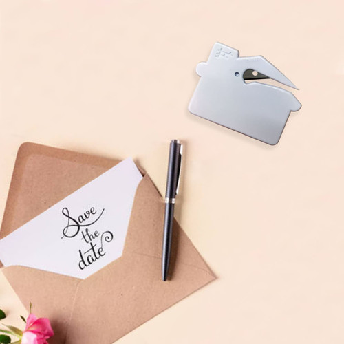 A silver house-shaped letter opener placed near an envelope and a pen, set against a soft background with flowers.