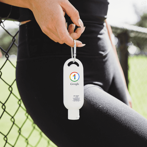 A white sunscreen bottle with a clip, featuring a logo, held by a person in dark activewear.