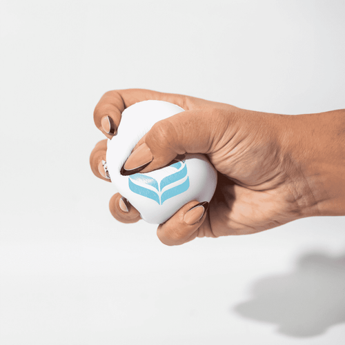 A white squeeze ball is being held, featuring a blue logo. The ball is shown being squeezed by a hand.