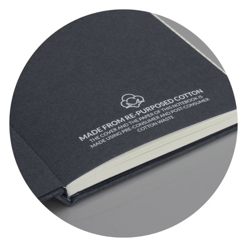 A recycled cotton hard cover notebook in dark grey with a logo, featuring cream-coloured pages inside.