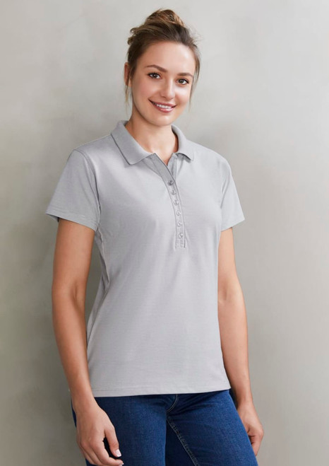 A light grey women's polo shirt with a button placket and a logo on the chest, styled with blue jeans.