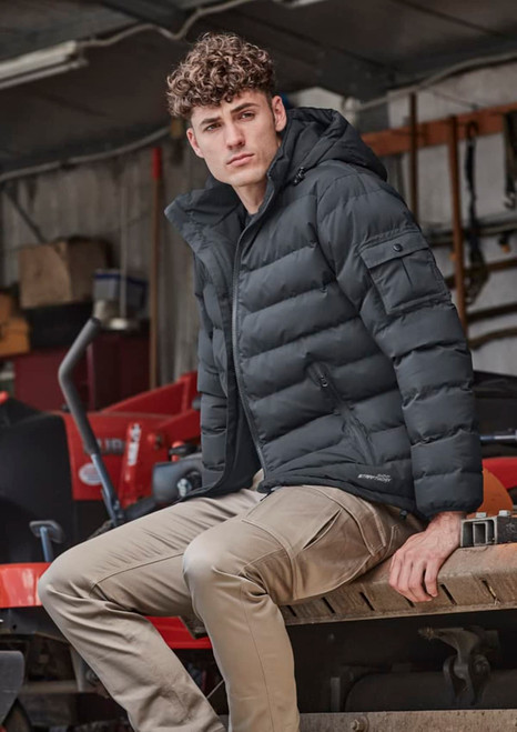A unisex hooded puffer jacket in black, featuring a fitted design and a logo, worn by a model sitting on machinery.