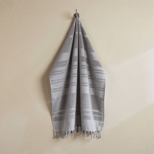 A flat terry towel in shades of grey, hanging neatly with fringed edges. It features a logo on the fabric.